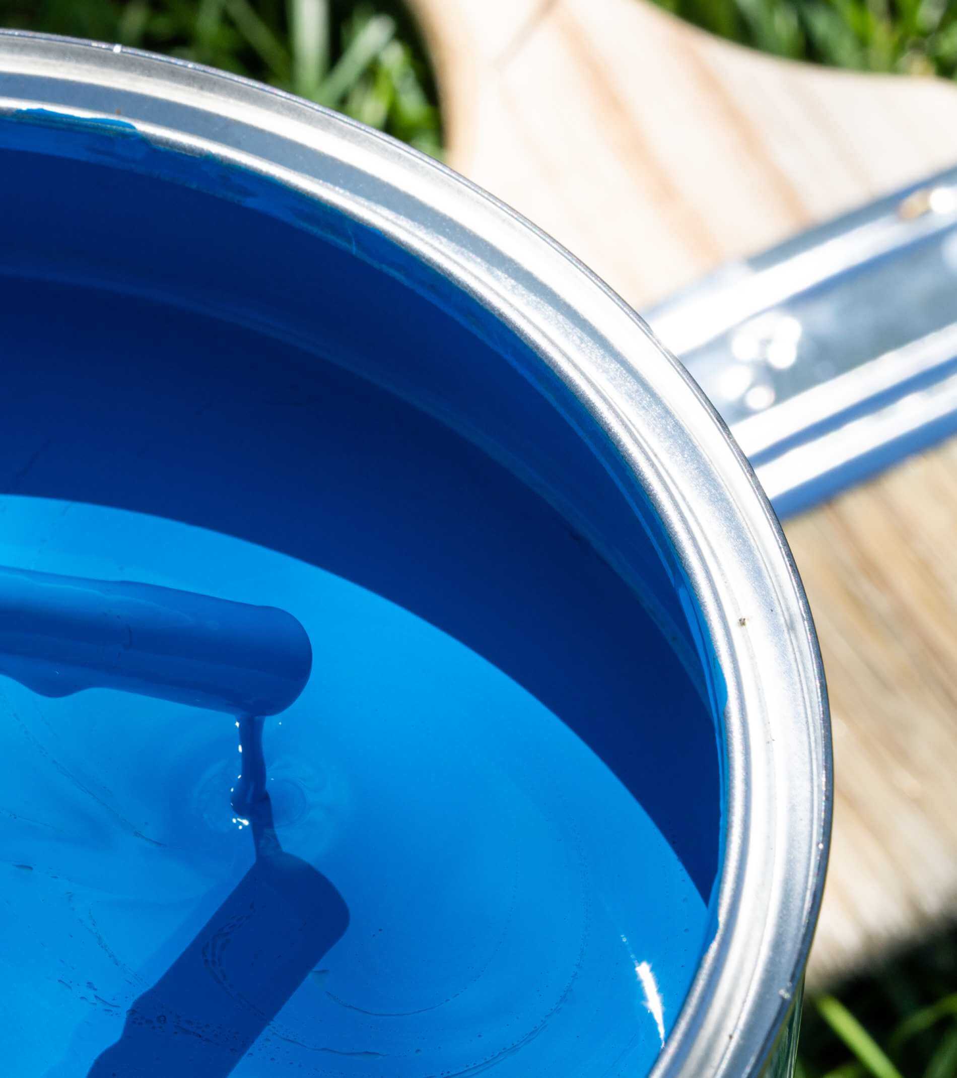 Top view of blue paint can, can lid, new brush on green grass